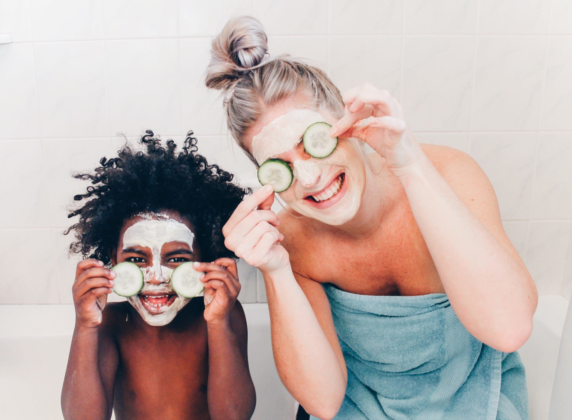 Woman and toddler smile with facemasks on holding cucumbers