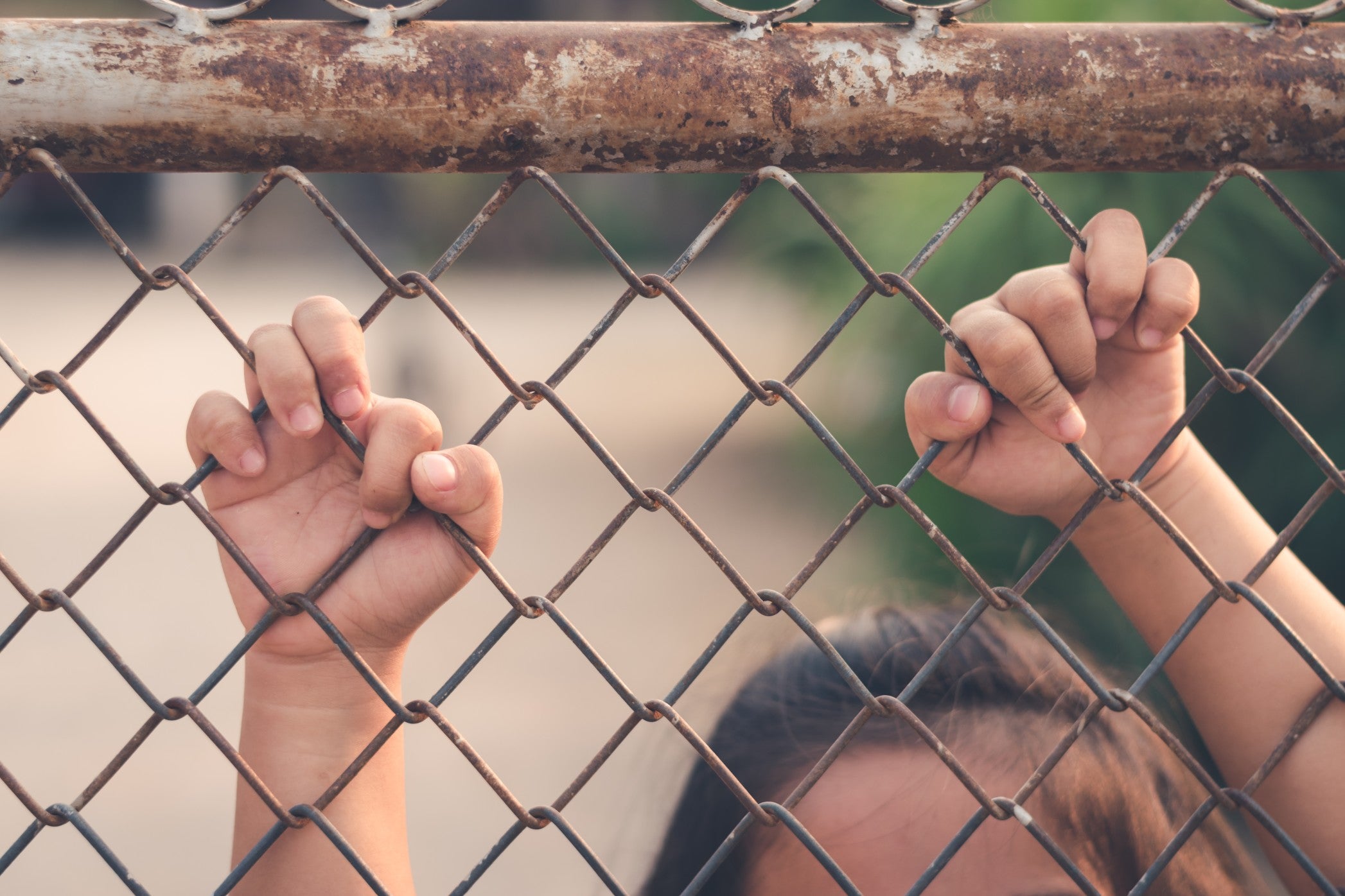 Kid holding hands behind metal fence
